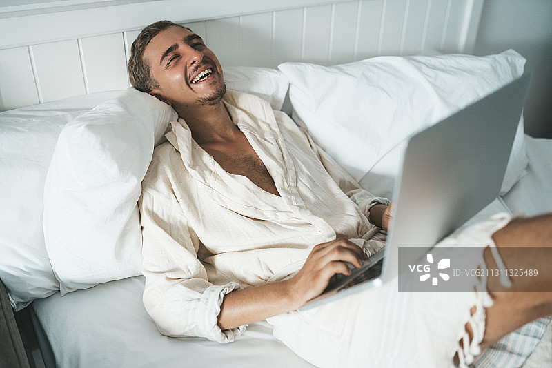 泰国清迈，一名白人男子在家工作，在床上放着笔记本电脑图片素材