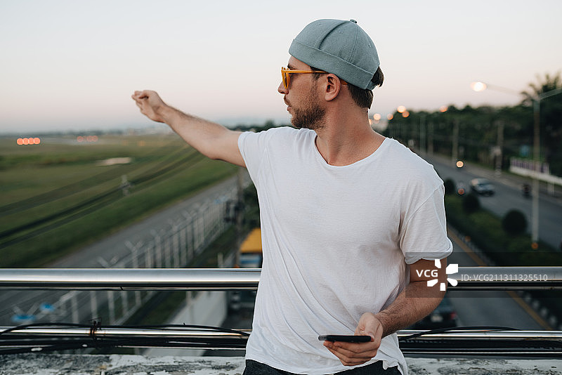 泰国清迈，一名戴着帽子和太阳镜的白人男子站在桥上使用智能手机图片素材