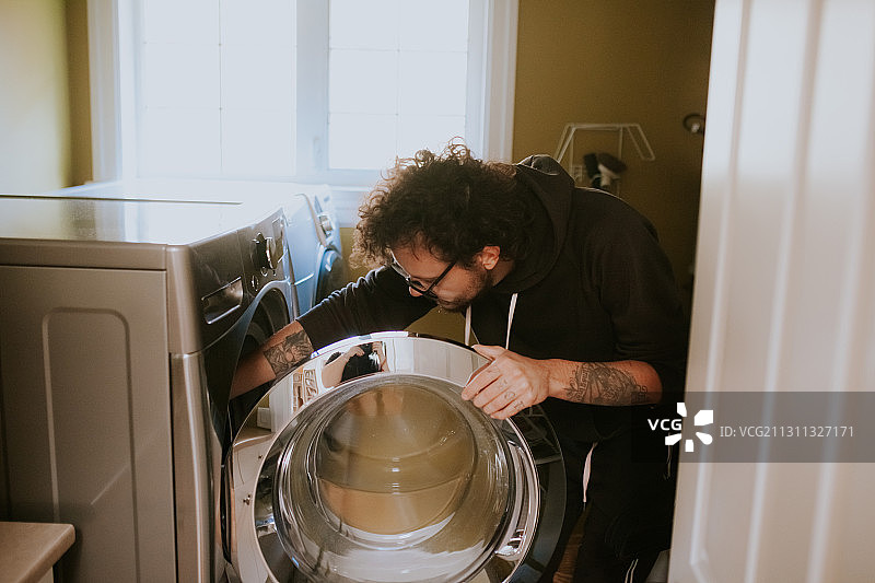 加拿大不列颠哥伦比亚省维多利亚，一名白人男子正在洗衣机上洗衣服图片素材