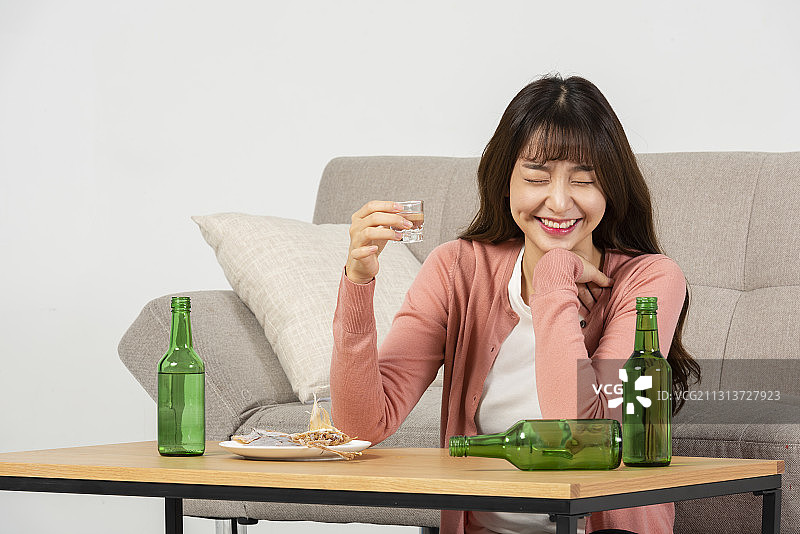 女人坐在桌边微笑着喝烧酒和零食在沙发前图片素材