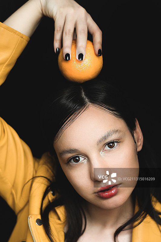 波斯尼亚和黑塞哥维那的萨拉伊波士那，一名年轻女子在黑色背景下举着橙色的头顶图片素材