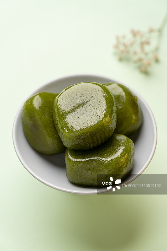 绿色纯色背景留白陶瓷高脚茶点盘上的绿色食品青团图片素材