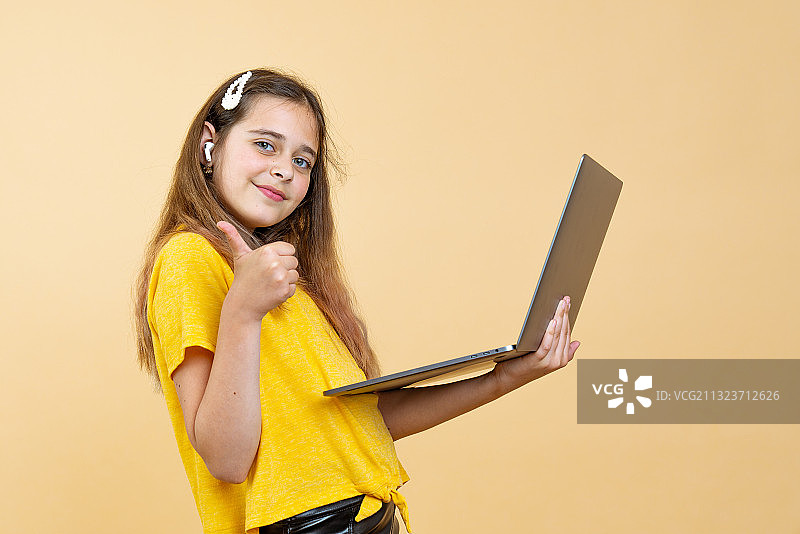 一个女孩拿着笔记本电脑，站在黄色背景下图片素材