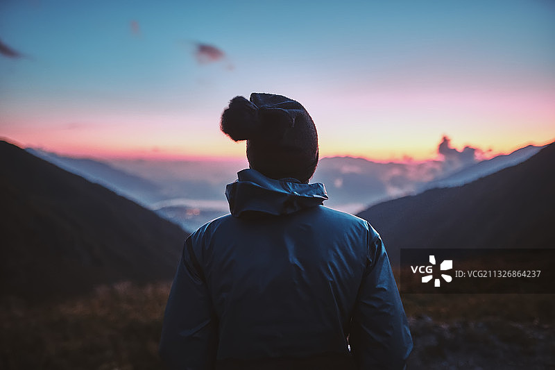 日落时分，一位身穿蓝色夹克的年轻徒步旅行者站在群山中图片素材