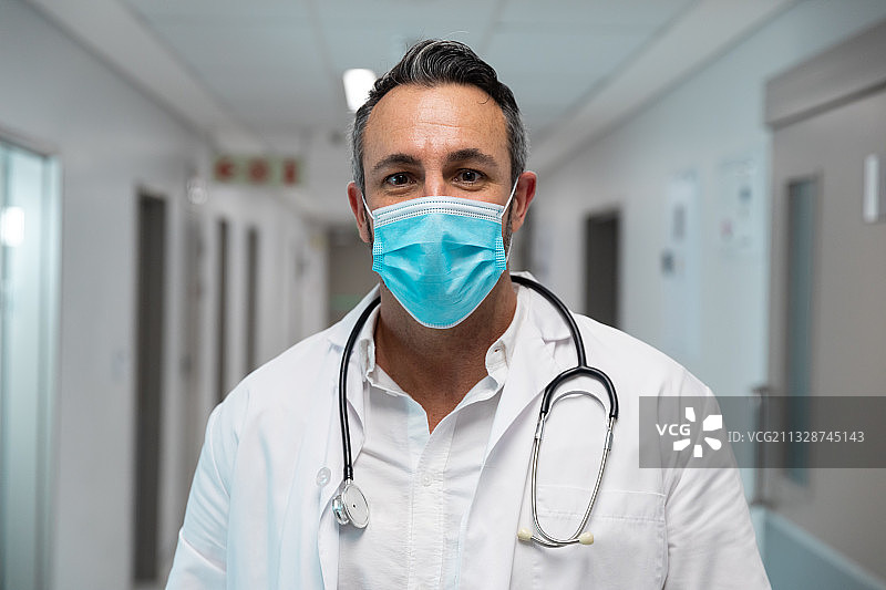 戴着口罩的混血男医生站在医院走廊里的肖像图片素材