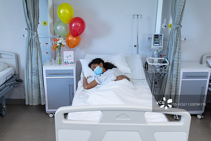 混血生病的女孩躺在医院的病床上，戴着口罩和指尖脉搏血氧计图片素材