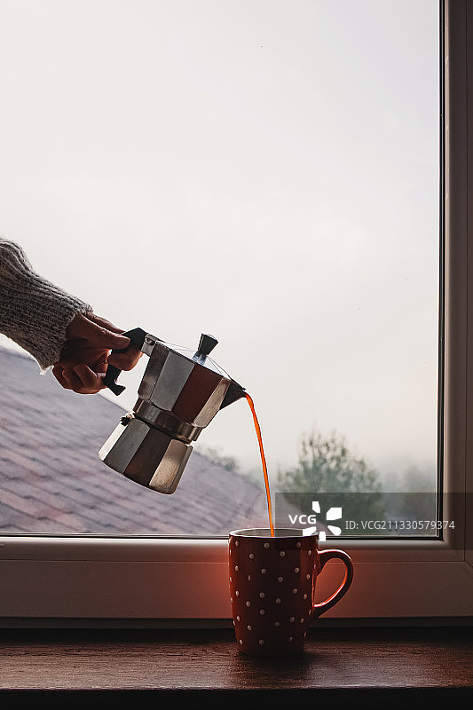 一个女人正用摩卡咖啡壶往窗边的杯子里倒咖啡图片素材