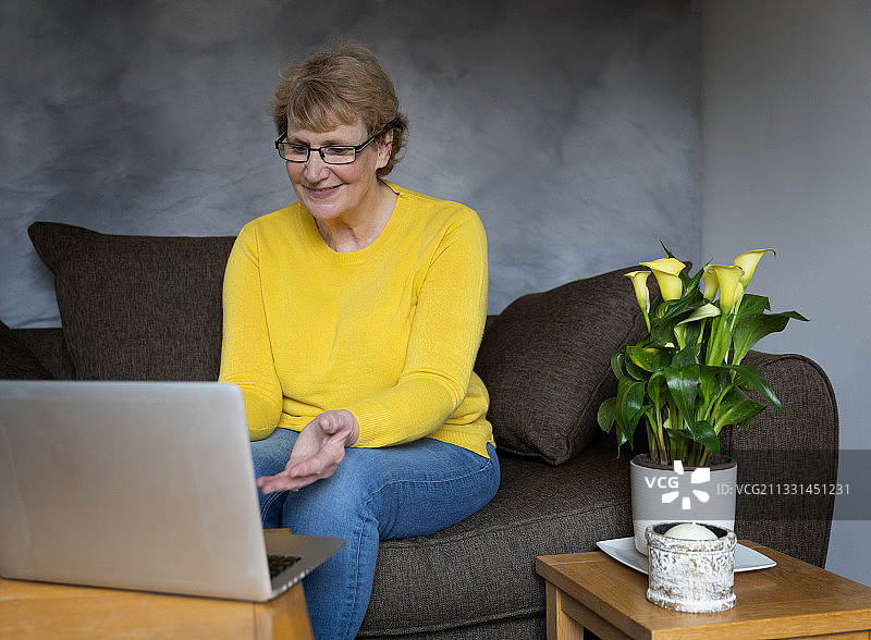微笑的成熟女人坐在家里的沙发上使用笔记本电脑，Galashiels，英国图片素材