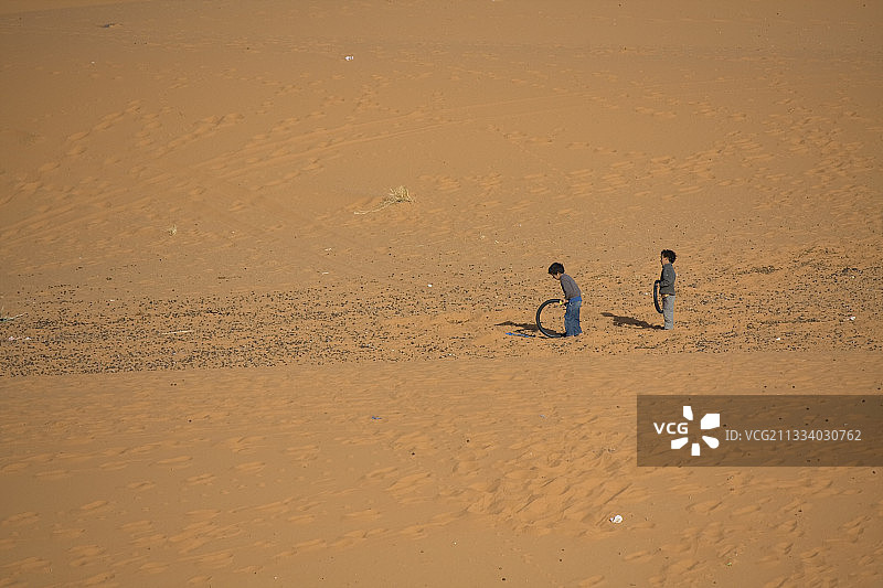 在摩洛哥的沙漠里，孩子们在推着一个轮子玩耍图片素材