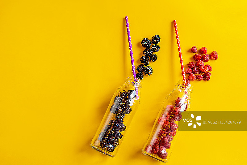 黑莓和覆盆子水果装在玻璃瓶里，用吸管涂在黄色上图片素材