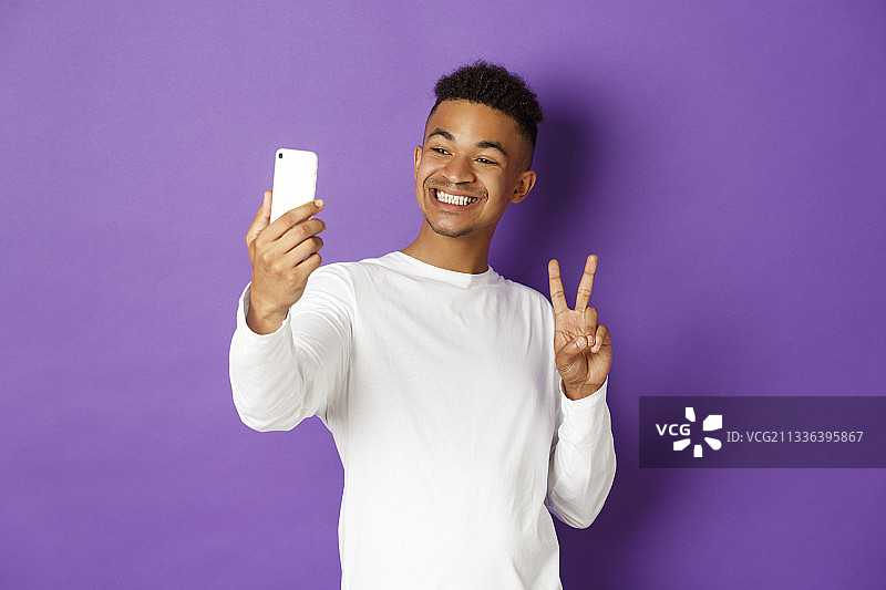 在紫色背景下站着的微笑的男人展示手机的肖像图片素材