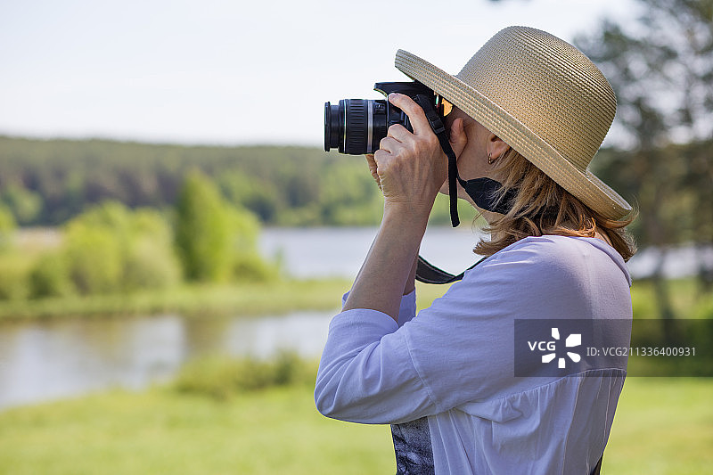 女子站在湖边用数码相机拍照的侧视图图片素材