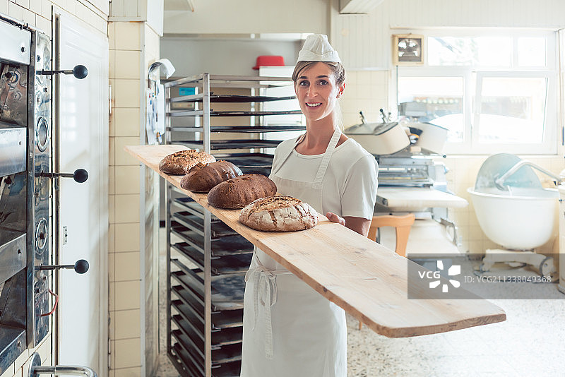 面包店里的一名女面包师骄傲地看着镜头，在展示面包图片素材