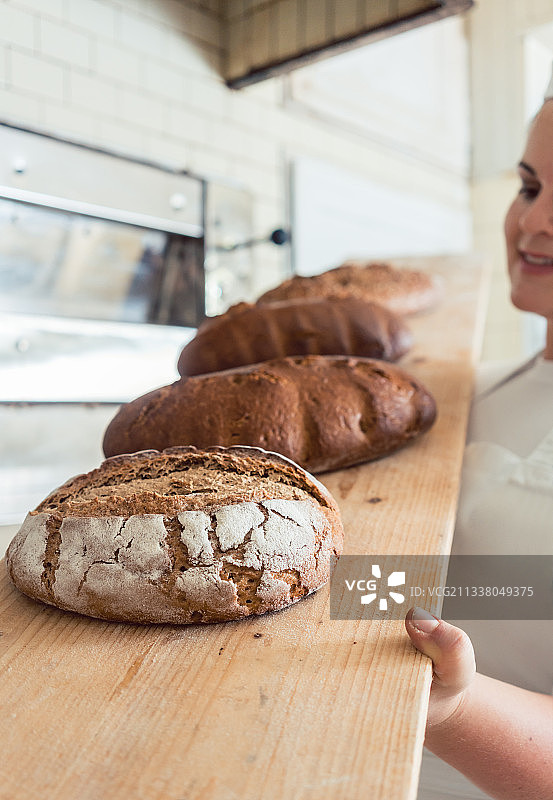 一位女面包师在一家面包店的板子上放着新鲜的面包图片素材