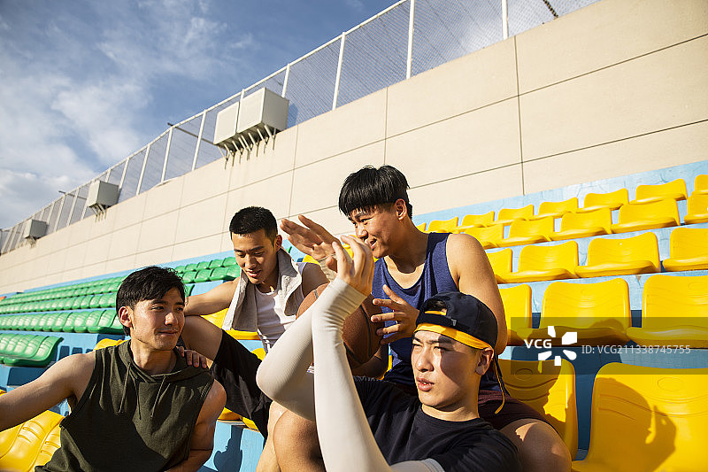 四个青年男子打篮球后坐在学校看台休息放松图片素材