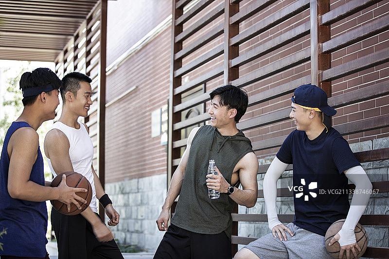 四个打篮球青年男子在学校走廊放松休息聊天图片素材