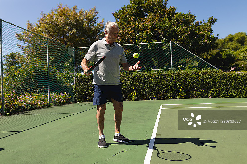 年长的白人男子在球场上拿着网球拍打网球图片素材