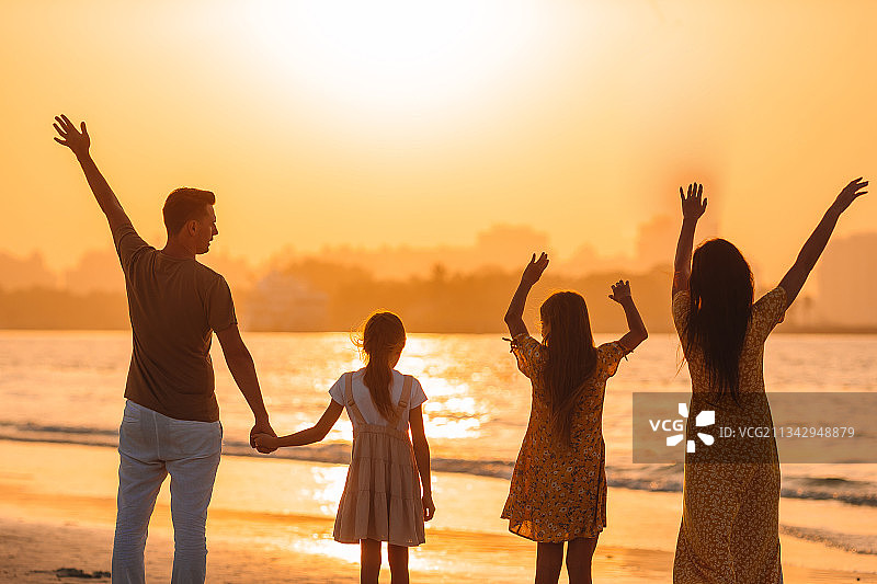 夕阳西下时，家人举着双臂站在海滩上图片素材