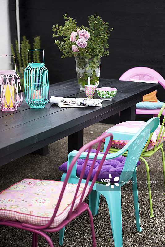 黑色木的桌上摆放着灯笼和玫瑰花束，四周是色彩鲜艳椅子和靠垫图片素材
