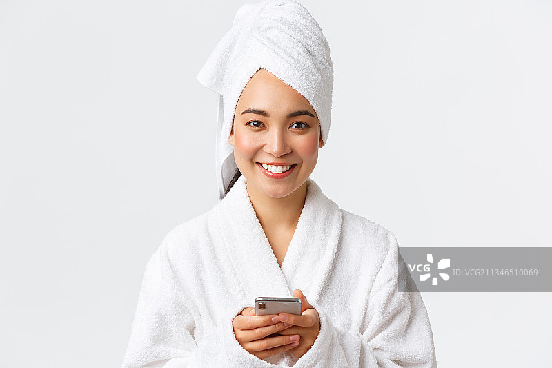 微笑的年轻女子的肖像穿着浴衣和毛巾在灰色的背景图片素材