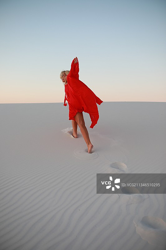 穿着红裙子的年轻女子在沙丘上行走图片素材