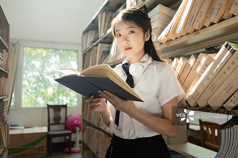 一个美女大学生在图书馆书架前拿着书图片素材