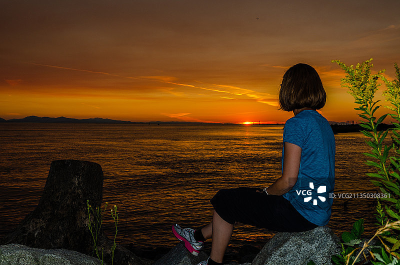加拿大不列颠哥伦比亚省温哥华，日落时分，坐在海边的岩石上的女人图片素材