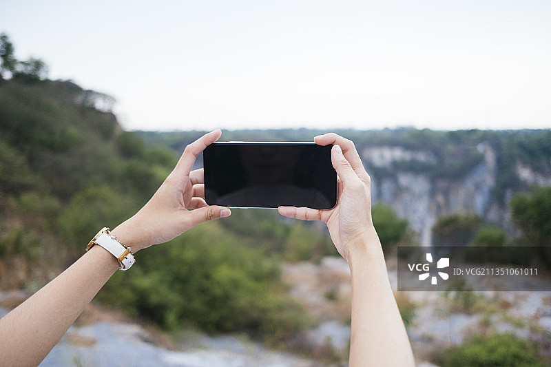 手拿智能手机的女人在山上拍照。图片素材