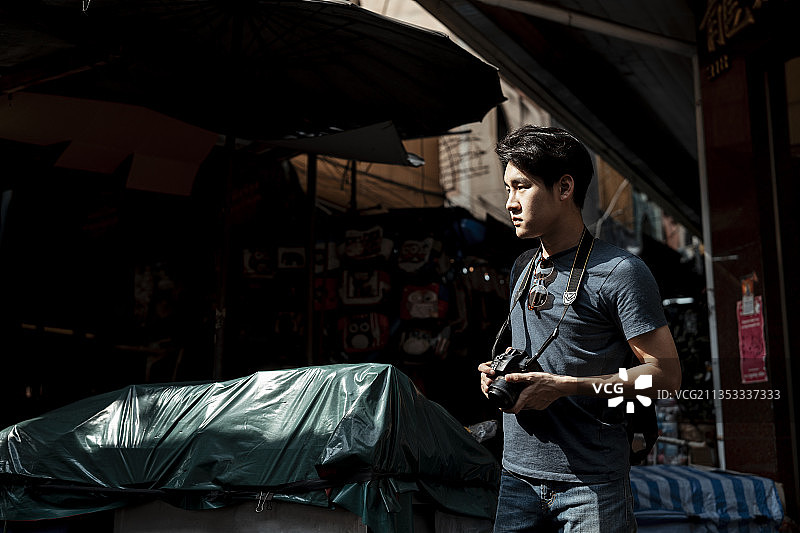 年轻英俊的亚洲摄影师男子在街头市场在曼谷。图片素材