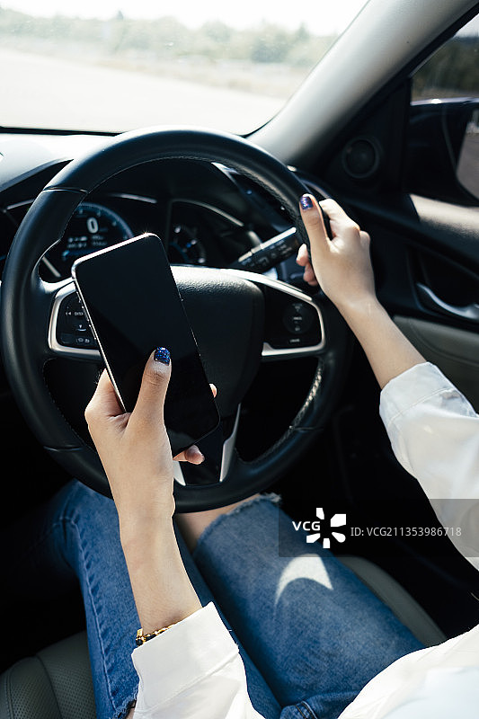 危险状况——女性在路上开车时使用智能手机。图片素材