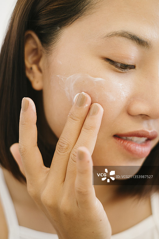 特写美丽的亚洲泰国女人短黑头发应用化妆品护肤霜在脸上。图片素材