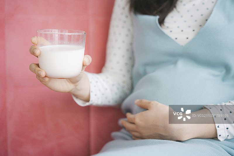 靠近年轻美丽的亚洲孕妇的手，抱着肚子和一杯牛奶。副本的空间。图片素材