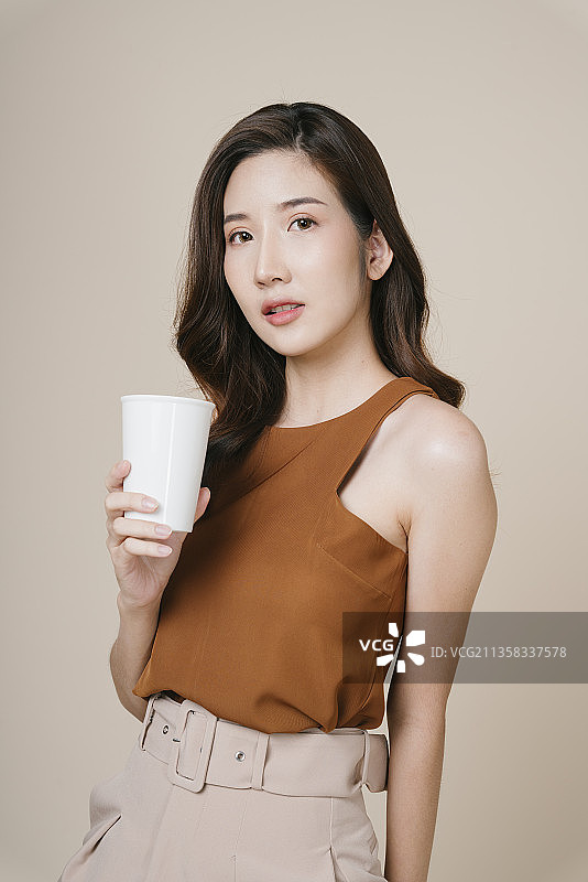 肖像的美丽年轻的亚洲妇女持有白色杯子为模拟。图片素材