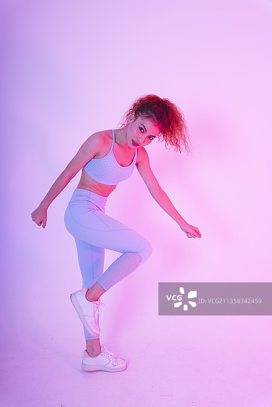 运动的年轻亚洲女人在健身装伸展身体在霓虹灯工作室灯光。健身房健身的概念。图片素材
