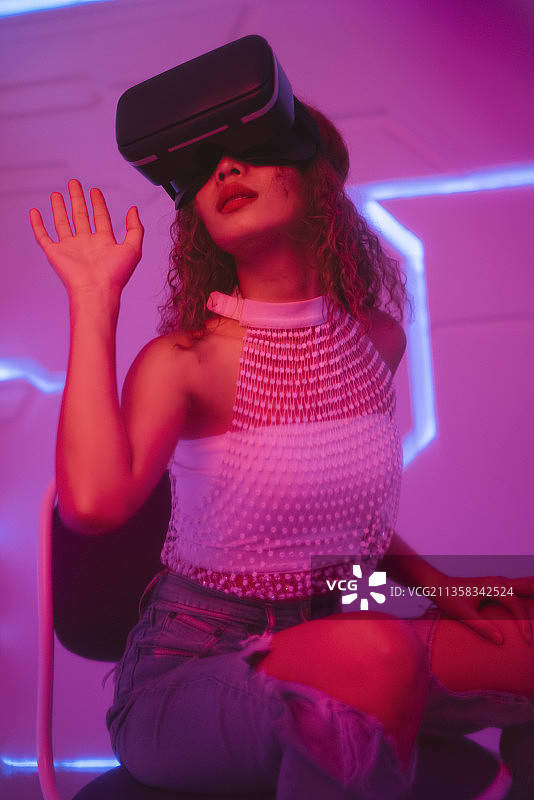 未来房间里戴着虚拟现实VR眼镜的模特年轻卷发女人。图片素材