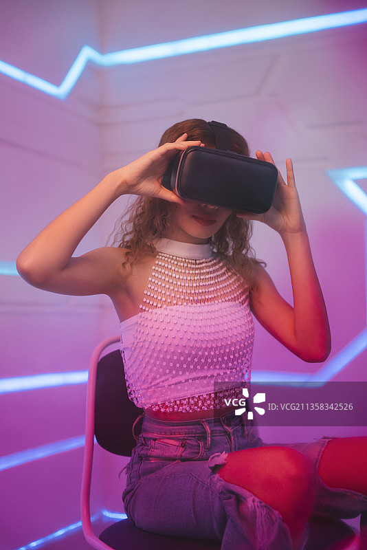 未来房间里戴着虚拟现实VR眼镜的模特年轻卷发女人。图片素材
