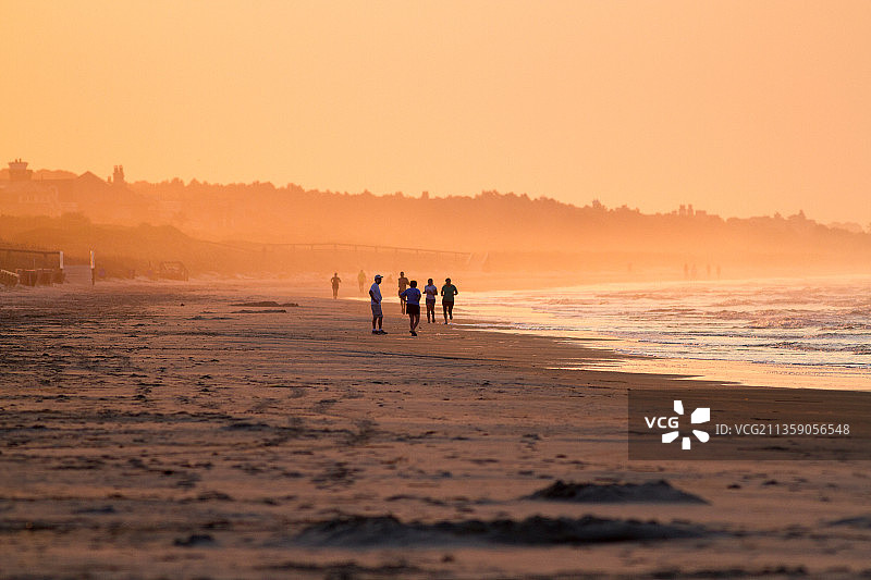 日落时，人们在海滩上对着天空散步图片素材
