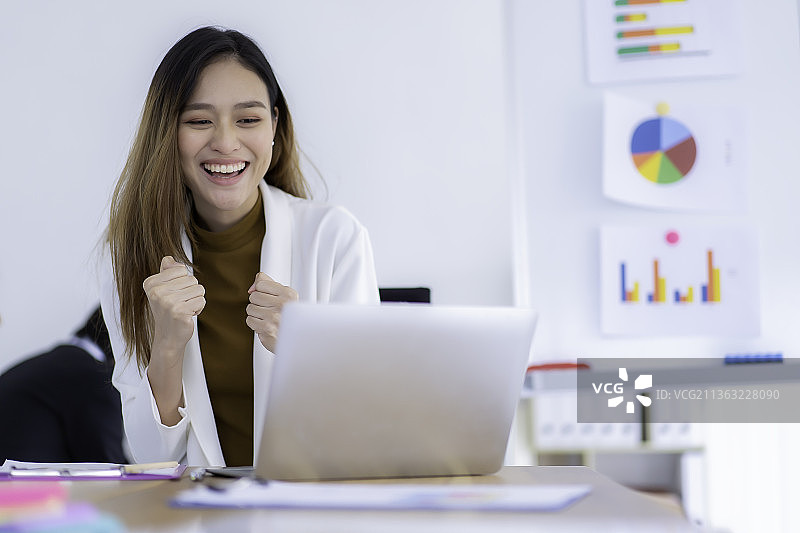 年轻的亚洲商业妇女工作，微笑的商业妇女使用笔记本电脑，而坐在办公室的办公桌图片素材