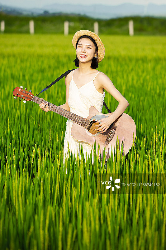 年轻女子在稻田里弹吉他图片素材