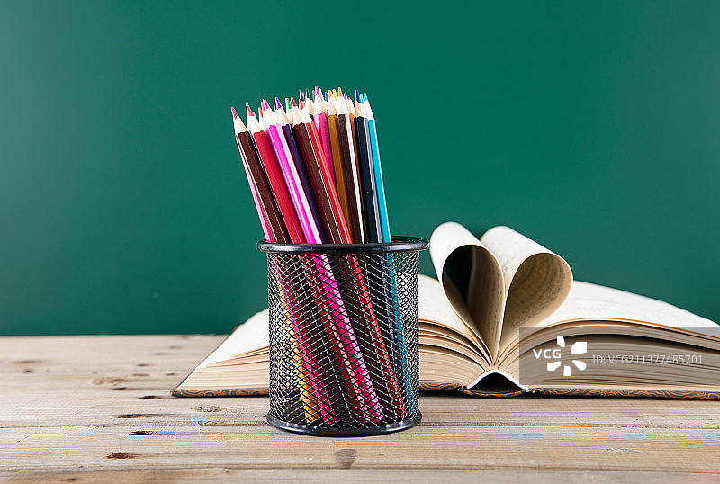 黑板前的讲桌上一本书页折成心形的书和装满笔筒的彩铅笔图片素材