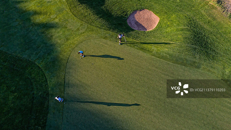 三名高尔夫球手在果岭上的俯视图图片素材