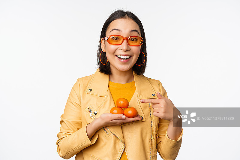 时尚快乐的亚洲女孩在太阳眼镜拿橘子和微笑图片素材