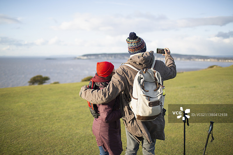 一对带着相机手机的徒步旅行者夫妇在悬崖上享受阳光明媚的海景图片素材