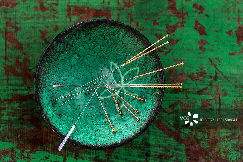 绿色陶瓷亚洲碗与针针灸在一个旧的绿色油漆木制板。图片素材