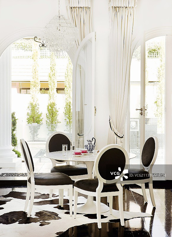 后现代的用餐区-白色的新洛可可椅子与黑色内饰，在拱形落地窗前，可以看到露台图片素材