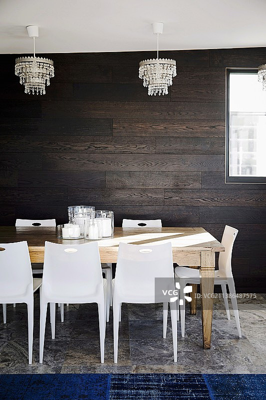餐厅的叠椅、大木桌、水晶吊灯、深色木墙和宝蓝色地毯铺在石灰华地板上图片素材