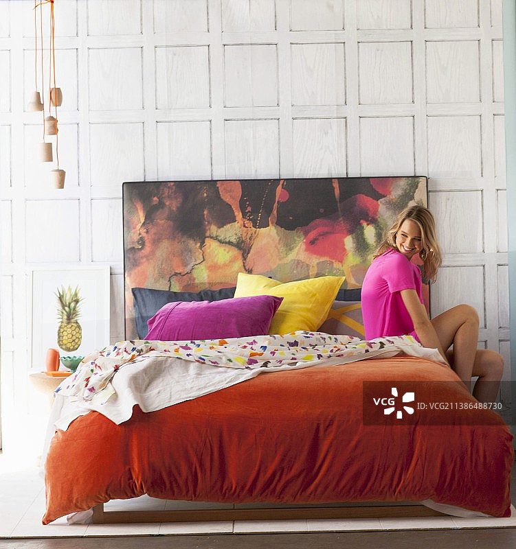 年轻女子在双人床与橙色天鹅绒盖和彩色床头板图片素材