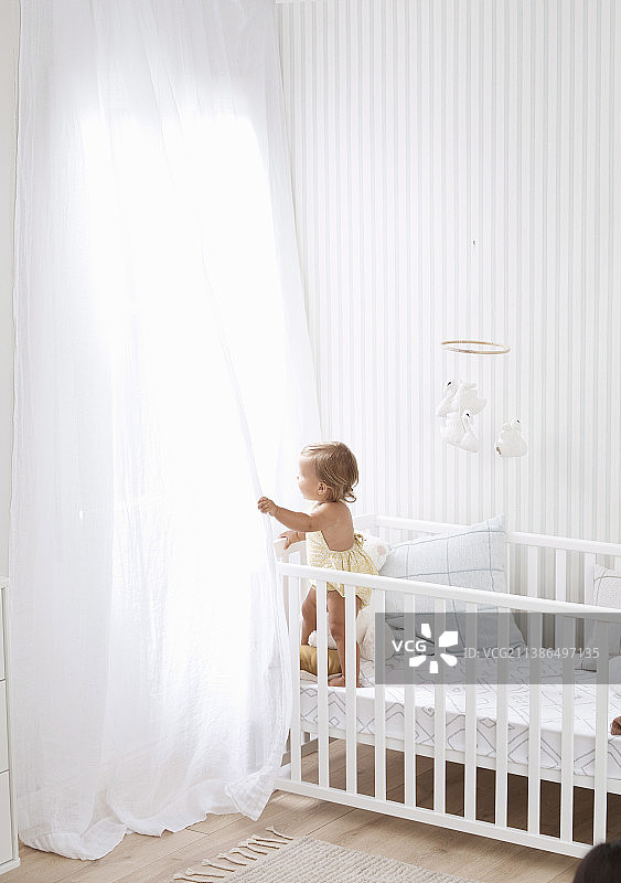 白色婴儿房，配有婴儿床和落地透明窗帘图片素材