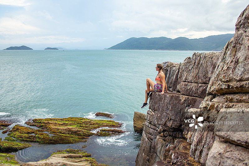 坐在海边岩石上的女人的后视图，圣卡塔琳娜州，巴西图片素材