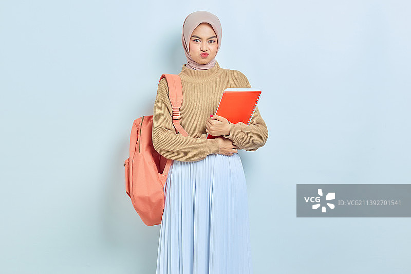 悲伤的年轻亚洲穆斯林女学生穿着棕色毛衣，背包里拿着书，看着镜头图片素材